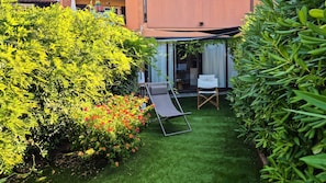 Un jardín bien cuidado con césped, una zona de estar con una silla y un edificio con puerta de cristal.