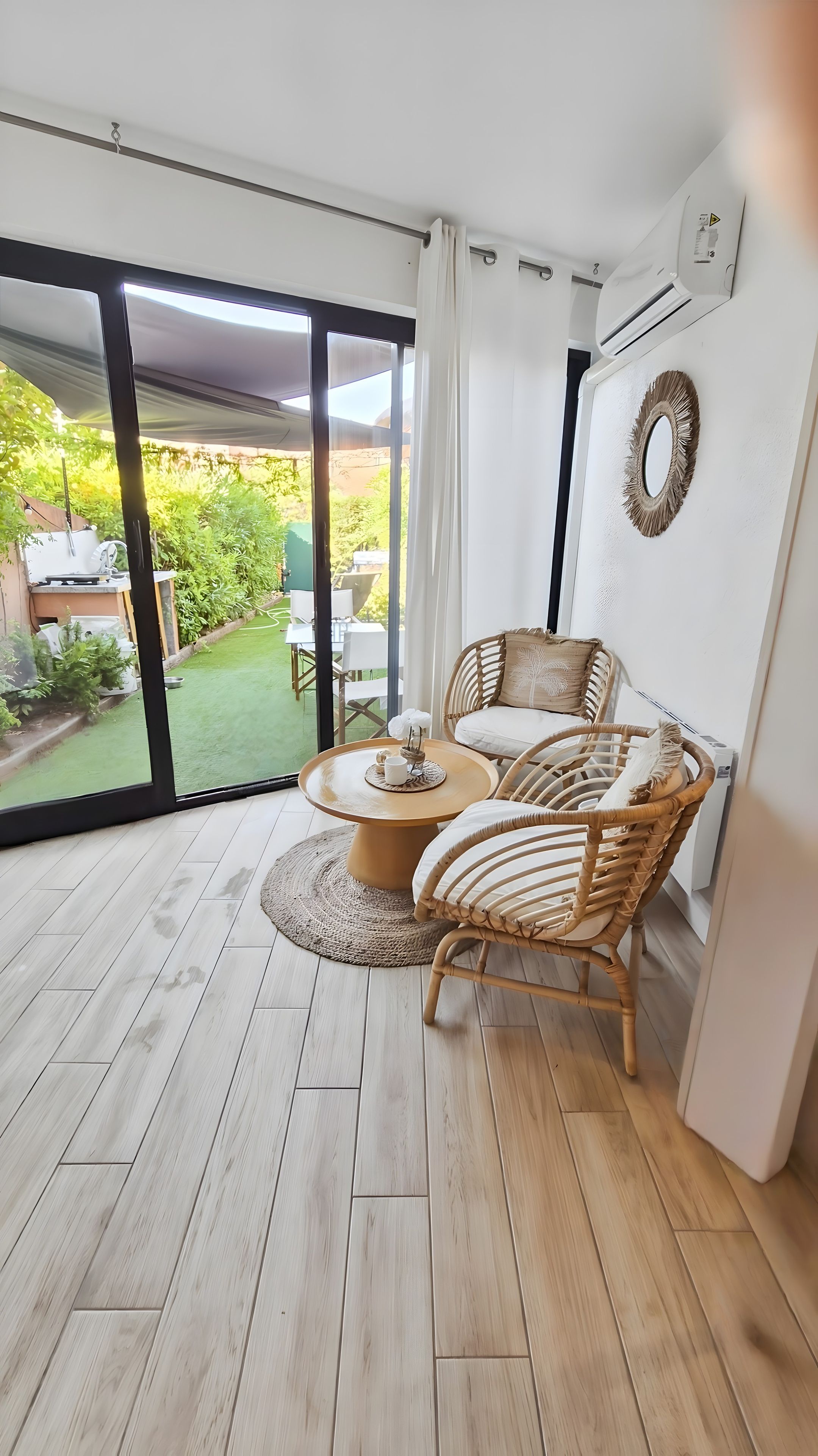 Ein Zimmer mit einer großen Schiebeglas-Tür, die zu einem Garten führt, einem runden Holztisch mit Stühlen und einer Wand-Klimaanlage.