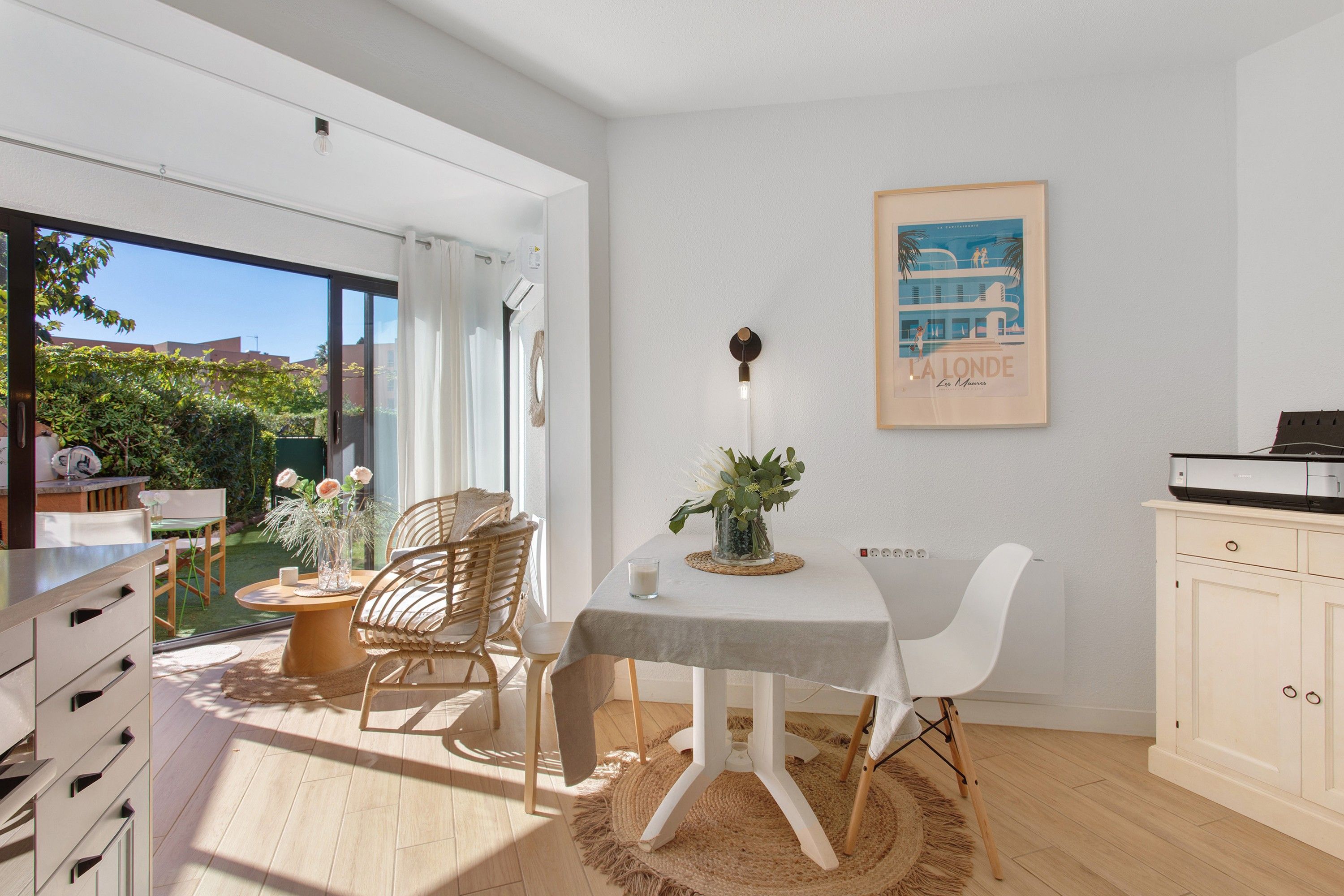 Une cuisine moderne avec des meubles blancs, un coin repas comprenant une table et des chaises, et une grande fenêtre donnant sur un paysage verdoyant.