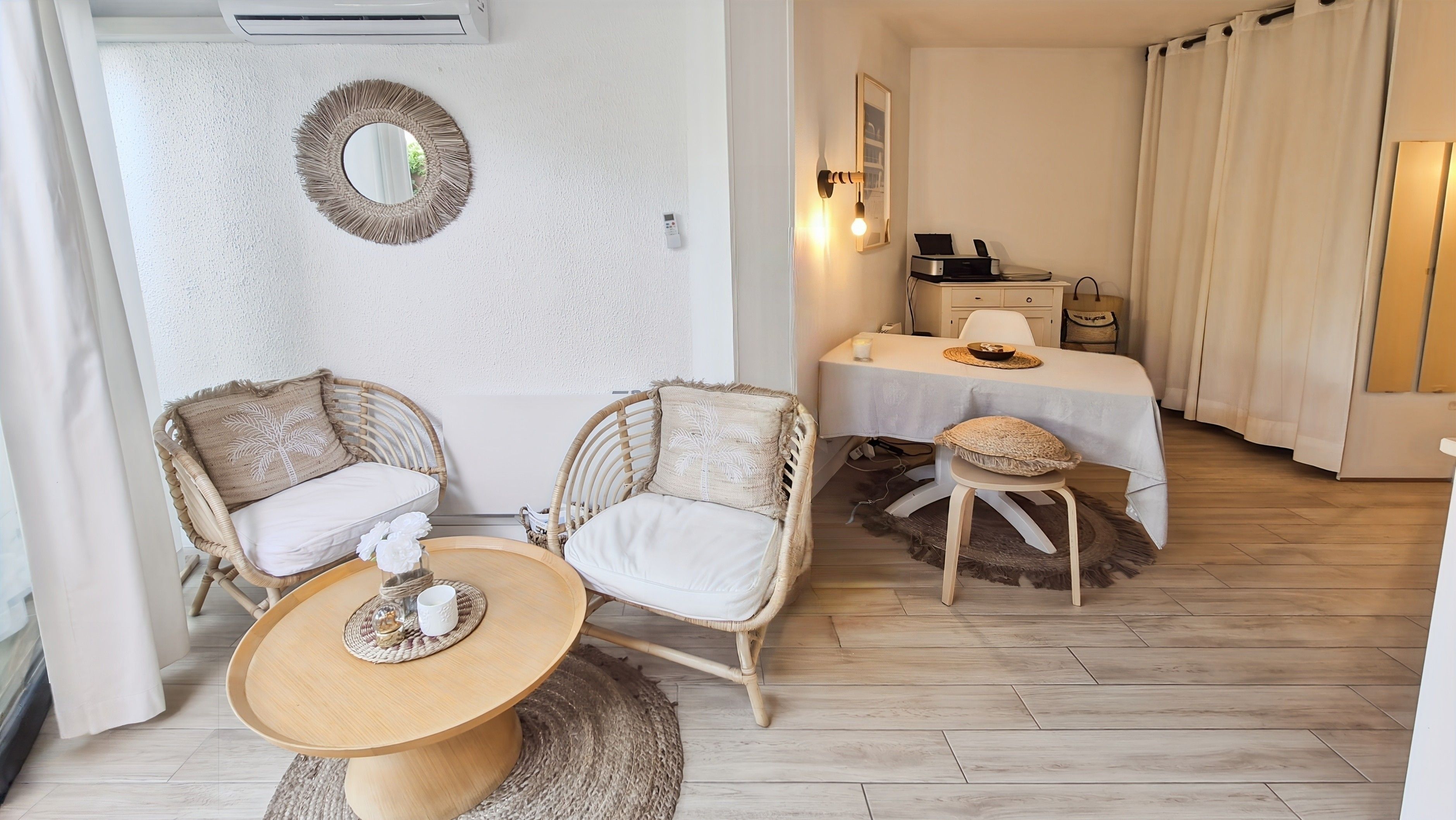 Een kamer met rieten meubilair, een ronde tafel, een bed met een witte dekbedovertrek en een spiegel aan de muur.