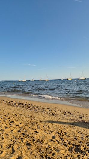 Una playa con arena dorada y varios veleros en el agua.