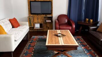 A living room with a sofa, a red chair, a coffee table, a TV mounted on a wooden wall, and a patterned rug.