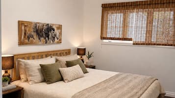 Un dormitorio con una cama de madera, una mesita de noche con lámpara, un cuadro en la pared y una ventana con persianas.