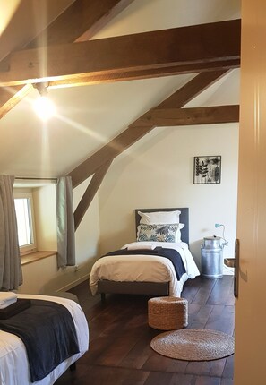 Quarto com teto inclinado, cama com cabeceira, mesa de cabeceira, janela com cortinas e radiador fixado na parede.