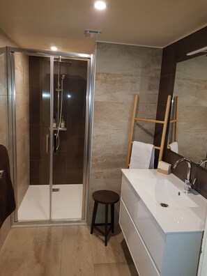 Uma casa de banho moderna com cabine de duche em vidro, toucador com espelho e um pequeno banquinho.