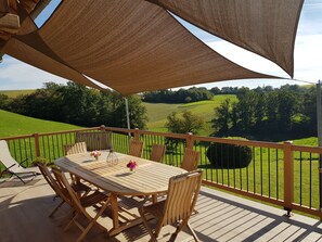 Um deck de madeira com mesa e cadeiras, com vista para uma paisagem verde.