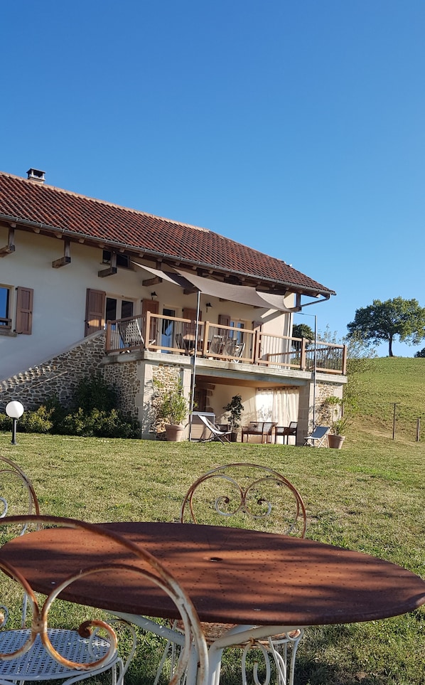 Uma casa de dois andares com varanda, escadaria de pedra e gramado.