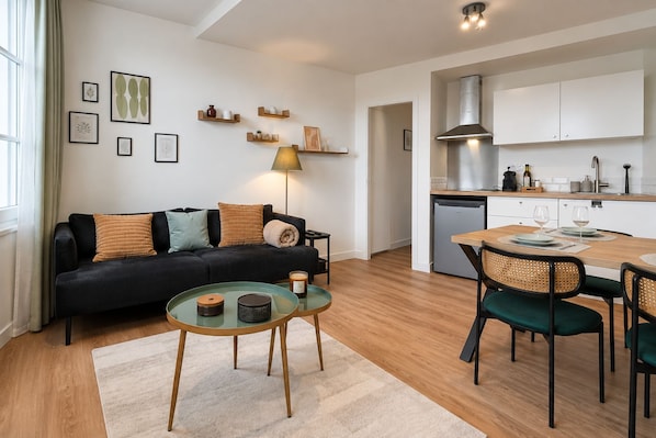 Ett modernt vardagsrum med en svart soffa, ett soffbord i glas och en matplats med ett bord och stolar i trä.