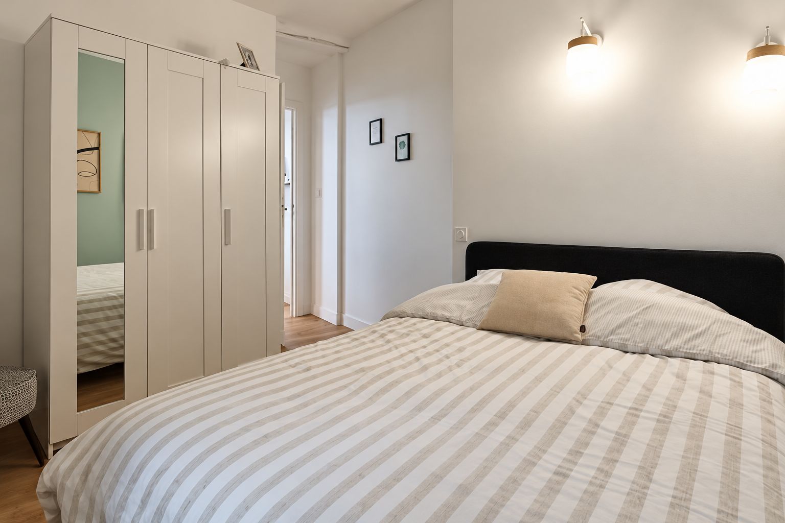 Quarto com cama, guarda-roupa e duas luzes fixadas na parede.
