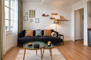 Ett modernt vardagsrum med en mörk soffa, två glasbord och en golvlampa.
