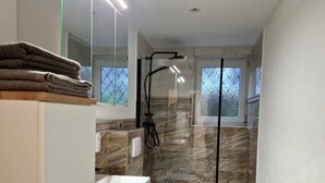 Un bany modern amb plat de dutxa envoltat de vidre, un lavabo blanc i un vàter.