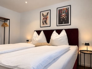 Una camera d'albergo con un letto matrimoniale, due cuscini, una testiera, due lampade a parete e due quadri incorniciati.