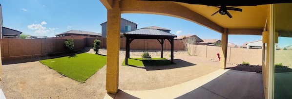 A covered patio area with a pergola, a small lawn, and a brick wall.