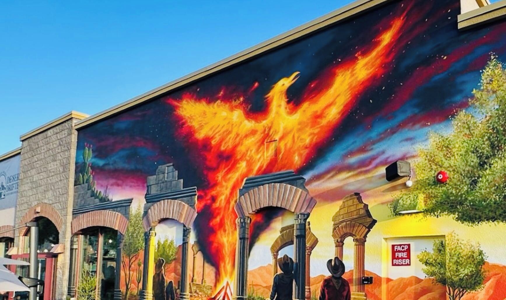 Un mural con un fénix llameante, arcos y un paisaje desértico.