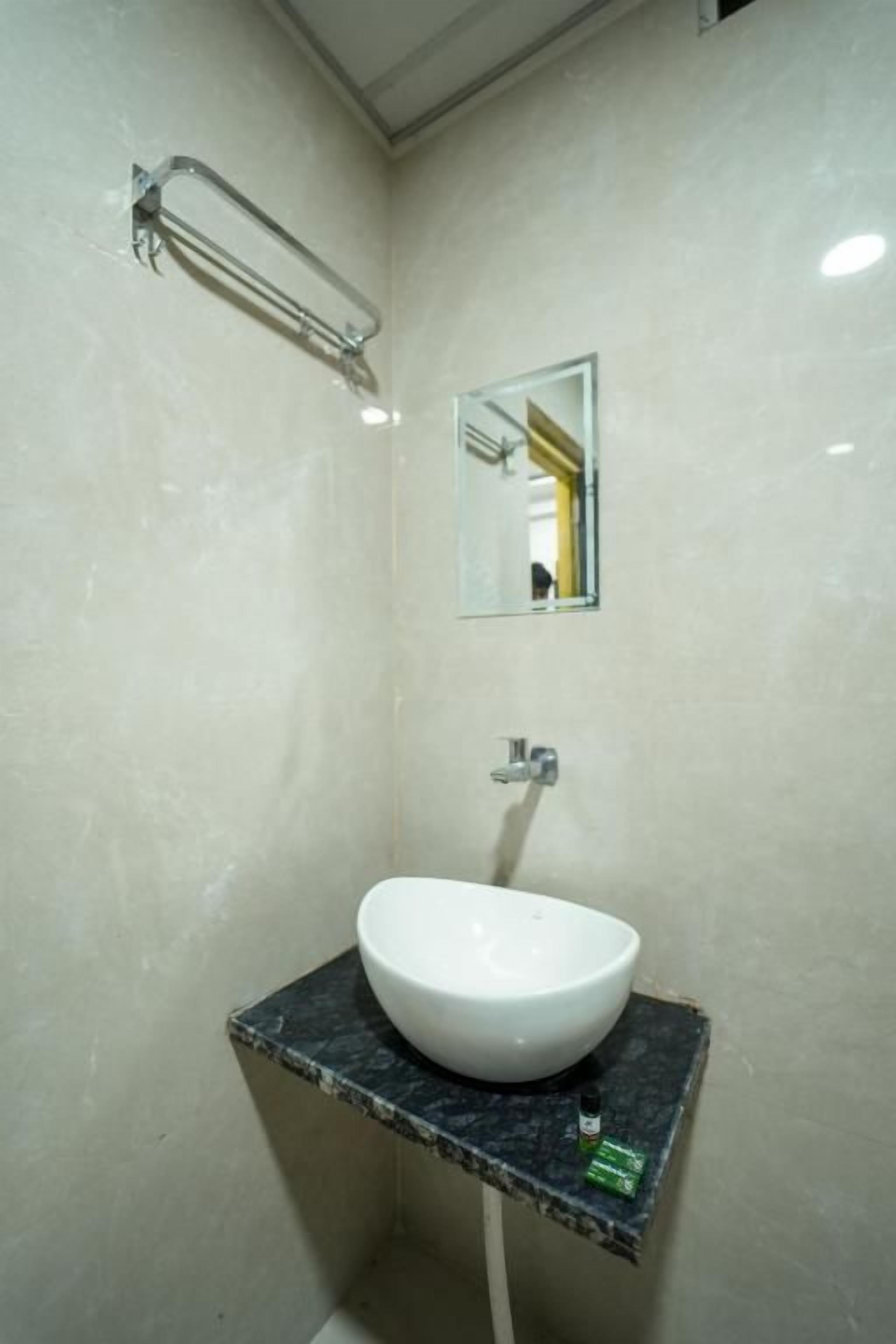 Une salle de bain avec un lavabo sur colonne blanc posé sur un plan de toilette foncé, un miroir au-dessus et un porte-serviettes fixé au mur.