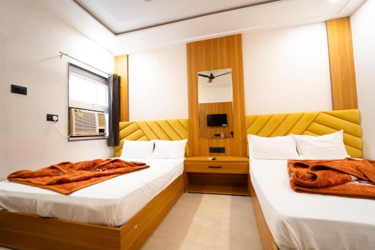 Habitació d'hotel amb dos llits, un panell de fusta al capçal, un mirall, un ventilador de sostre i un aparell d'aire condicionat.