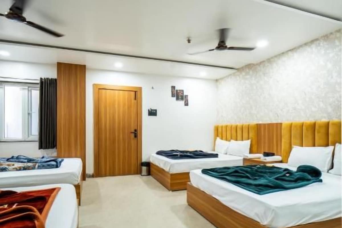 Habitació d'hotel amb dos llits, un capçal de llit de fusta, un ventilador de sostre i una porta que dona a una altra habitació.