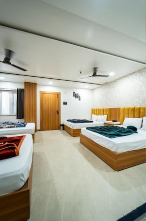 Habitació d'hotel amb dos llits, un capçal de llit de fusta, un ventilador de sostre i una porta que dona a una altra habitació.