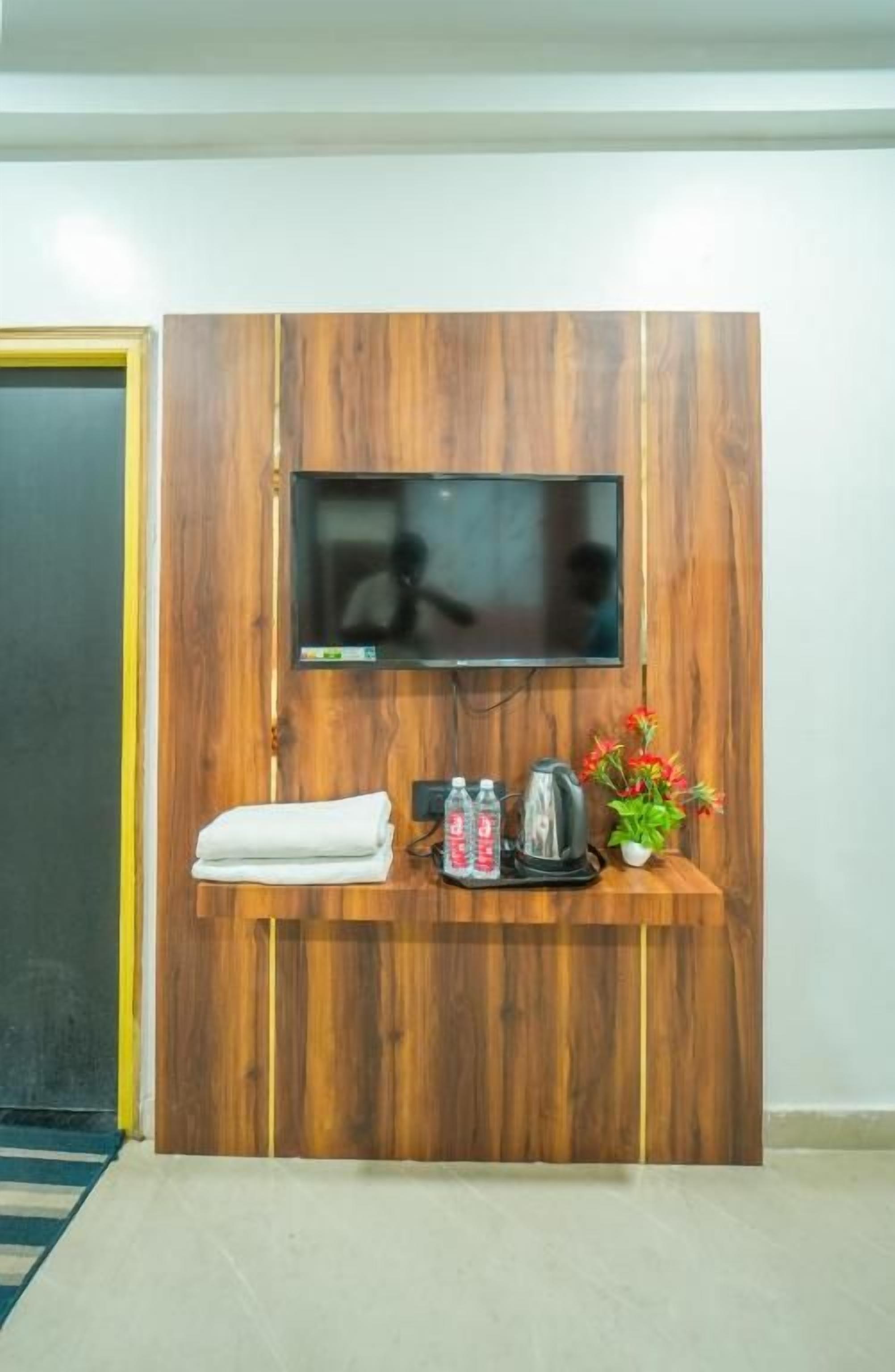 Un mostrador de recepción de madera con un televisor de pantalla plana, una tetera, una planta pequeña y una toalla doblada.