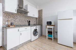 A compact kitchen with white cabinets, a built-in washing machine, a microwave, and a refrigerator. - Home2Book Betty Modern Studio in Puerto (Puerto del Rosario)