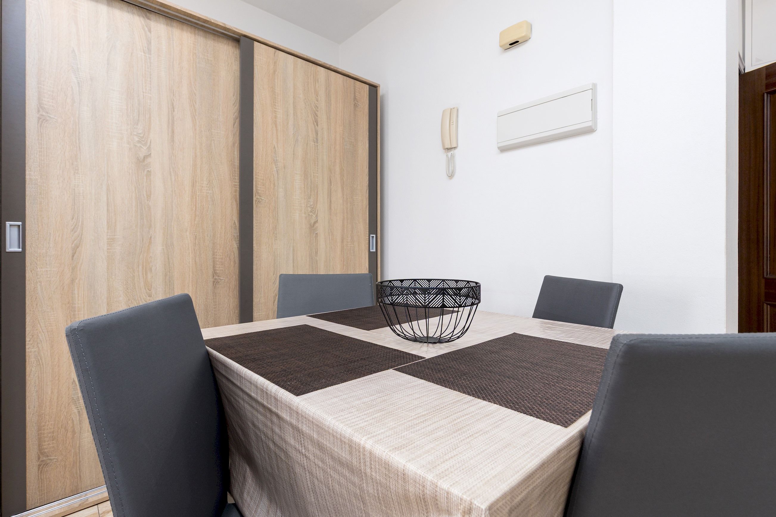 A dining area with a table set for four, two chairs on each side, a patterned table runner, and a black woven chair center.