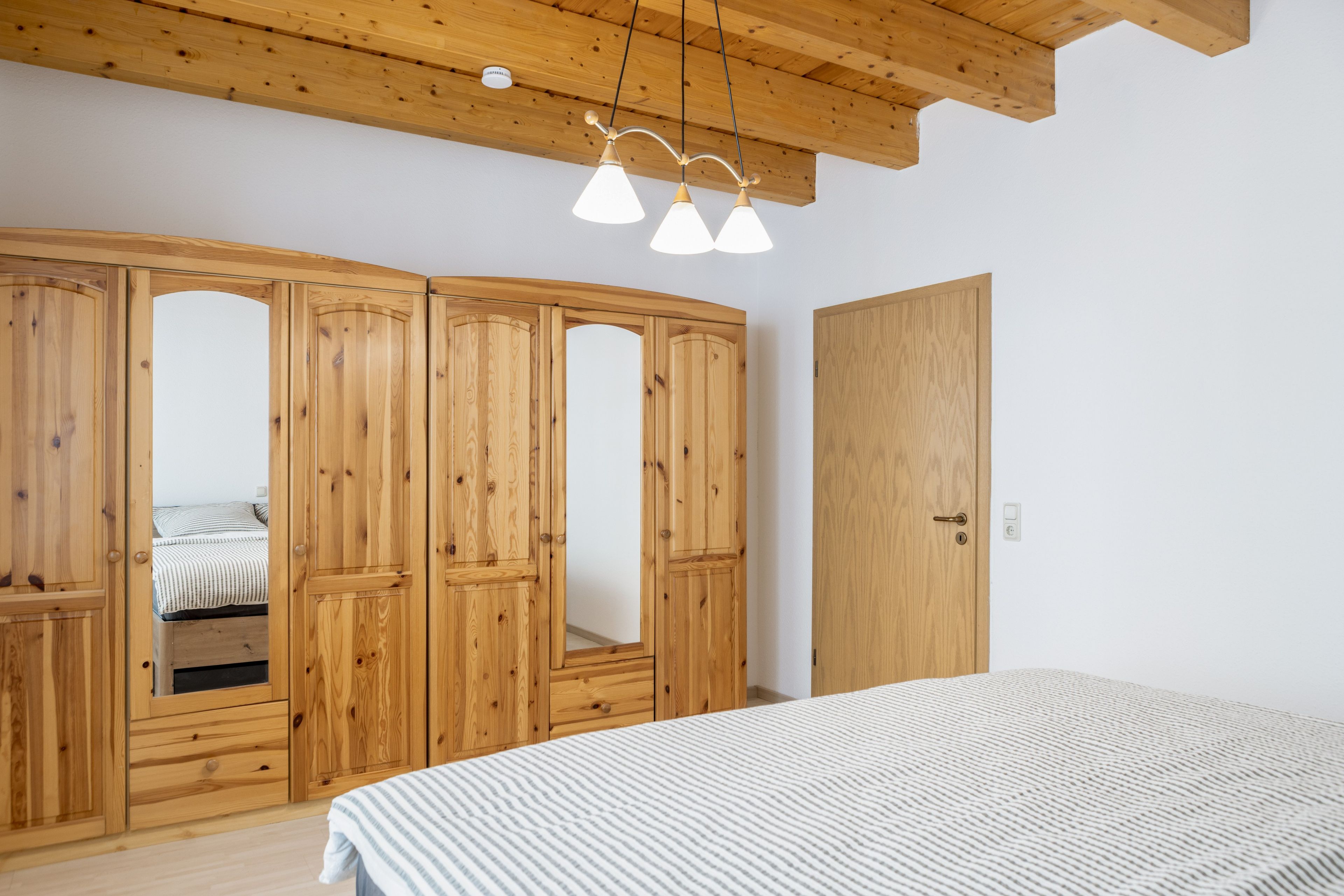 Ein Schlafzimmer mit einem Holzkleiderschrank, einem Bett mit gestreifter Bettwäsche und einer Deckenleuchte.