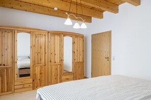 A bedroom with a wooden wardrobe, a bed with striped bedding, and a ceiling light fixture. - Apartment 'Unterhaun' with Private Garden and Wi-Fi (Hauneck)