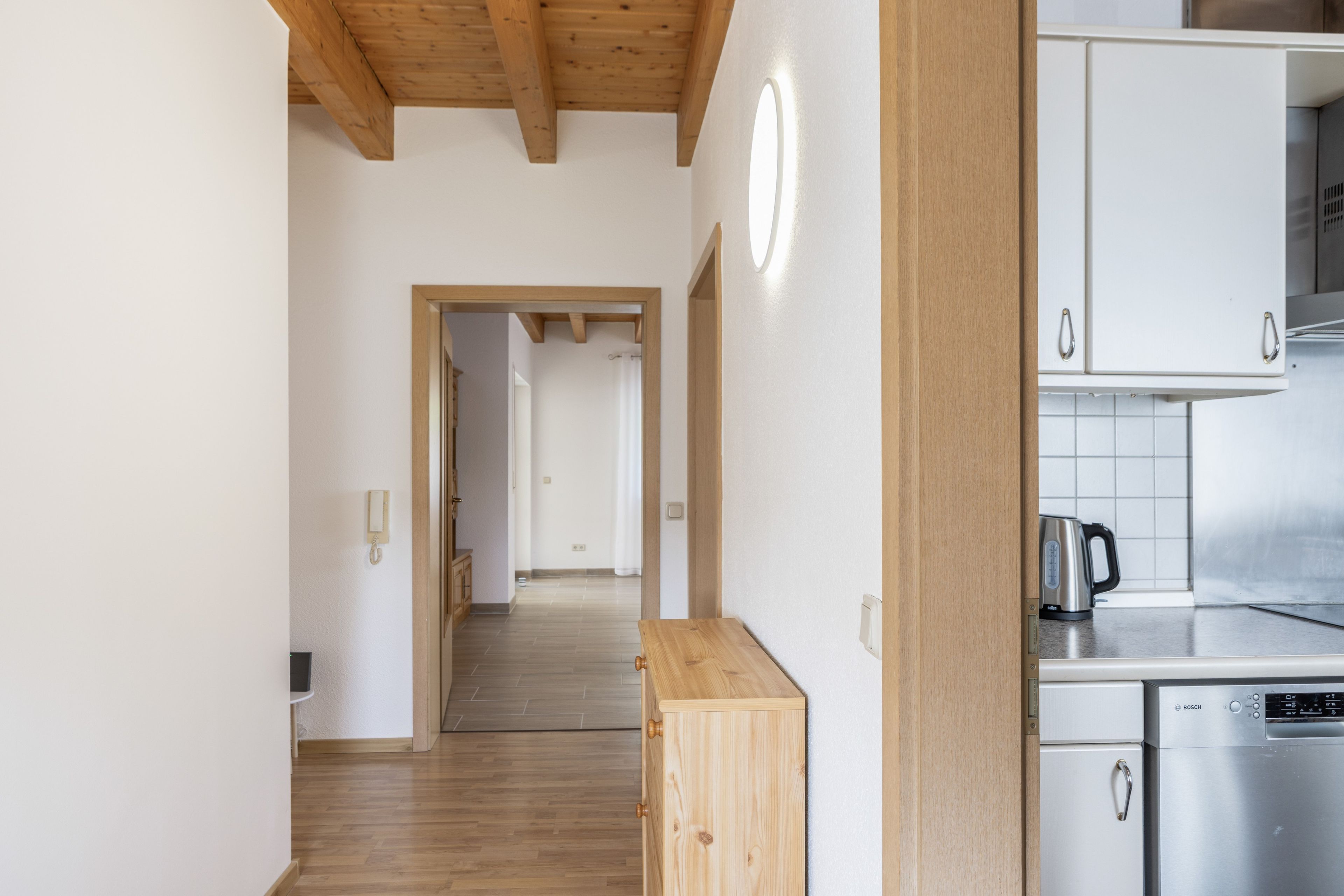 A modern kitchen with stainless steel appliances, wooden cabinets, and a herringbone-patterned floor.