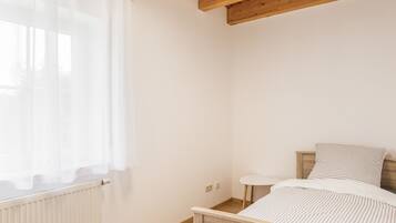 Une chambre à coucher avec une tête de lit en bois, un lit simple, une petite table de chevet et une fenêtre ornée de rideaux légers.