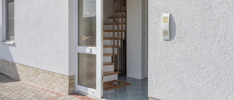 A residential entrance with a glass door, a wooden staircase, and a mailbox on the wall.
