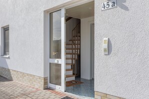 Een inkomhal van een wooncomplex met een glazen deur, een houten trap en een brievenbus aan de muur.