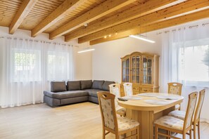 A room with a wooden ceiling, a grey sectional sofa, a wooden dining table with chairs, and a cabinet with glass doors. - Apartment 'Unterhaun' with Private Garden and Wi-Fi (Hauneck)