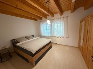 Een slaapkamer met een houten bed, een klein tafeltje, een kast en een raam met gordijnen.