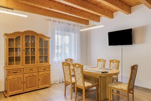 Een eetgedeelte met een houten tafel en stoelen, een kast met glazen deuren en een flatscreen televisie aan de wand bevestigd.