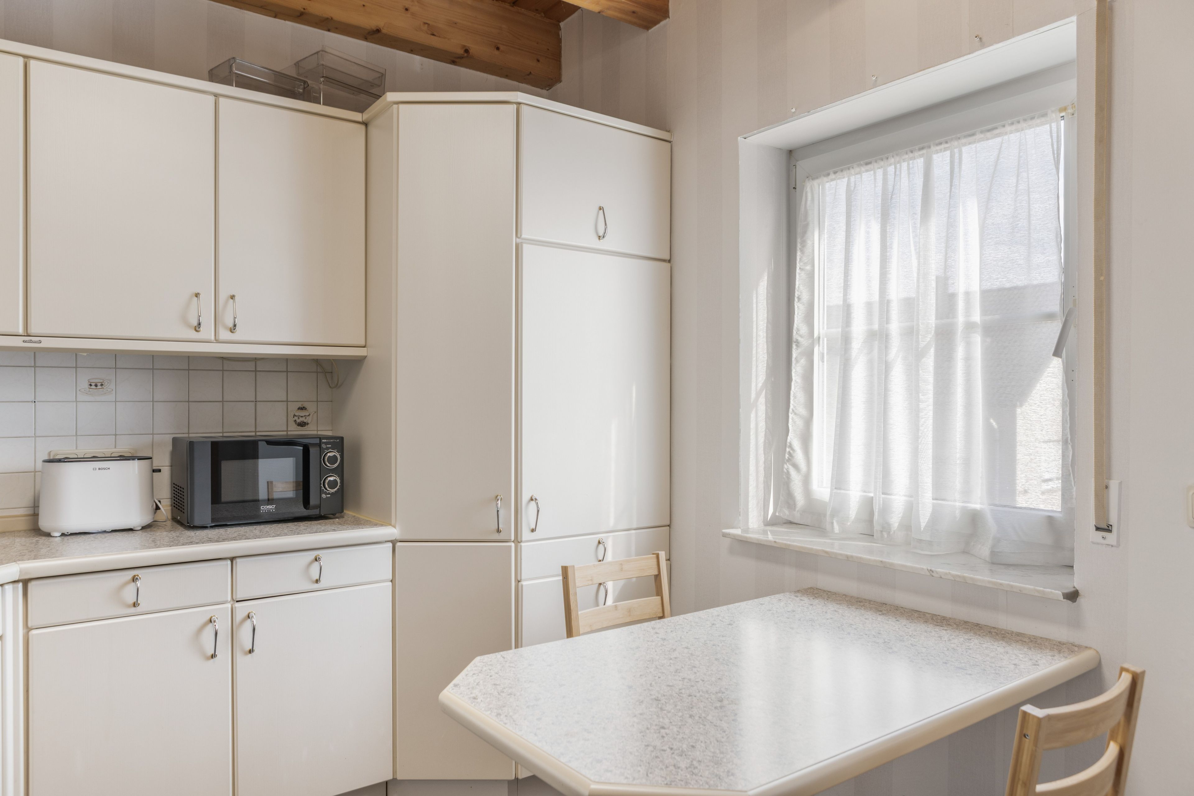 A kitchen with white cabinets, a microwave, and a window with sheer curtains.