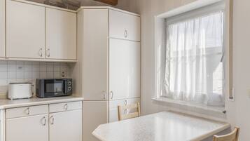 Une cuisine avec des meubles blancs, un four à micro-ondes et une fenêtre ornée de rideaux légers.