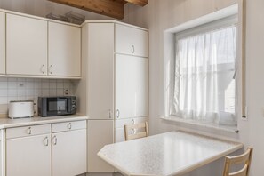 A kitchen with white cabinets, a microwave, and a window with sheer curtains.