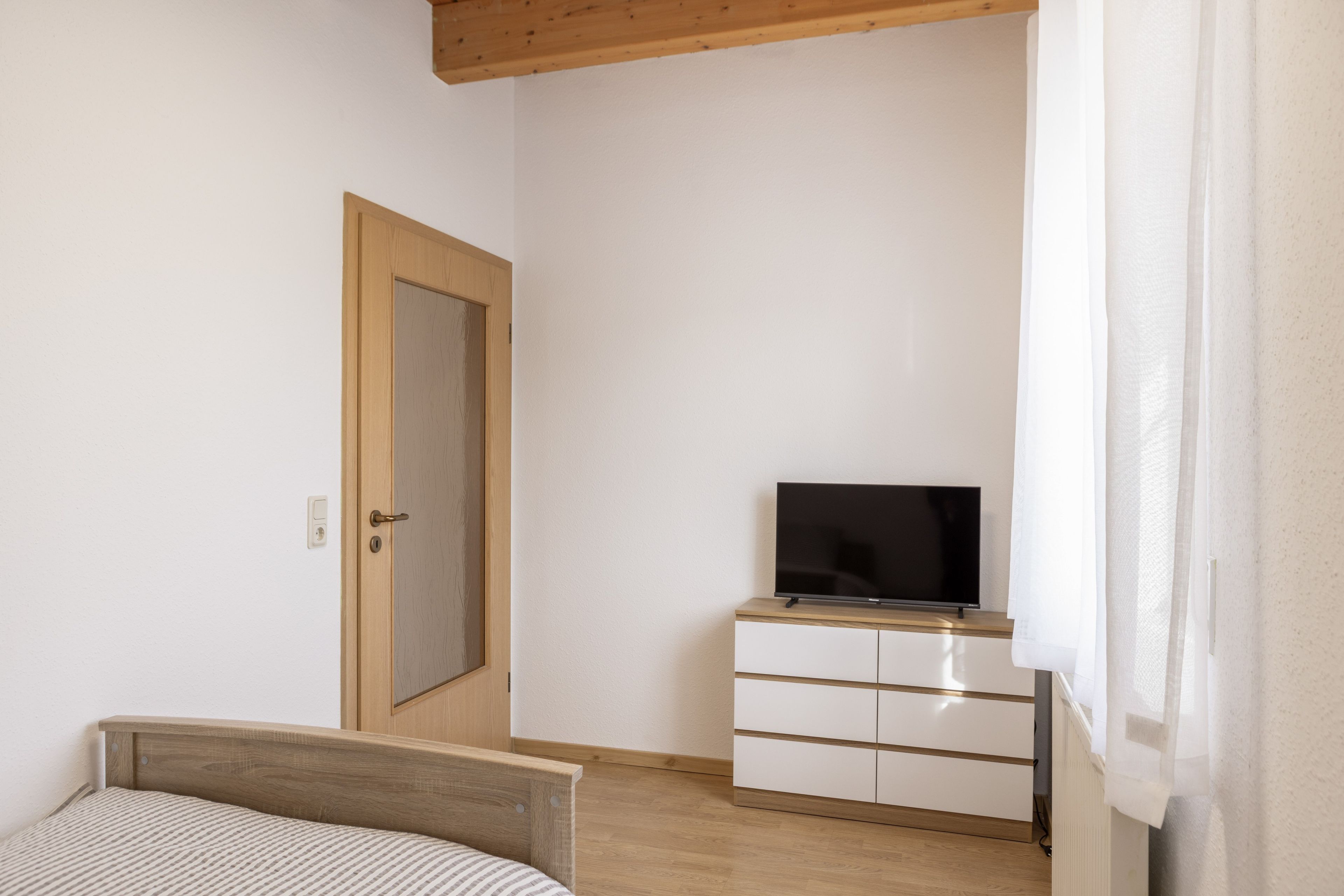 Ein Schlafzimmer mit einem Bett, einem Fernseher auf einer Kommode und einer Tür.