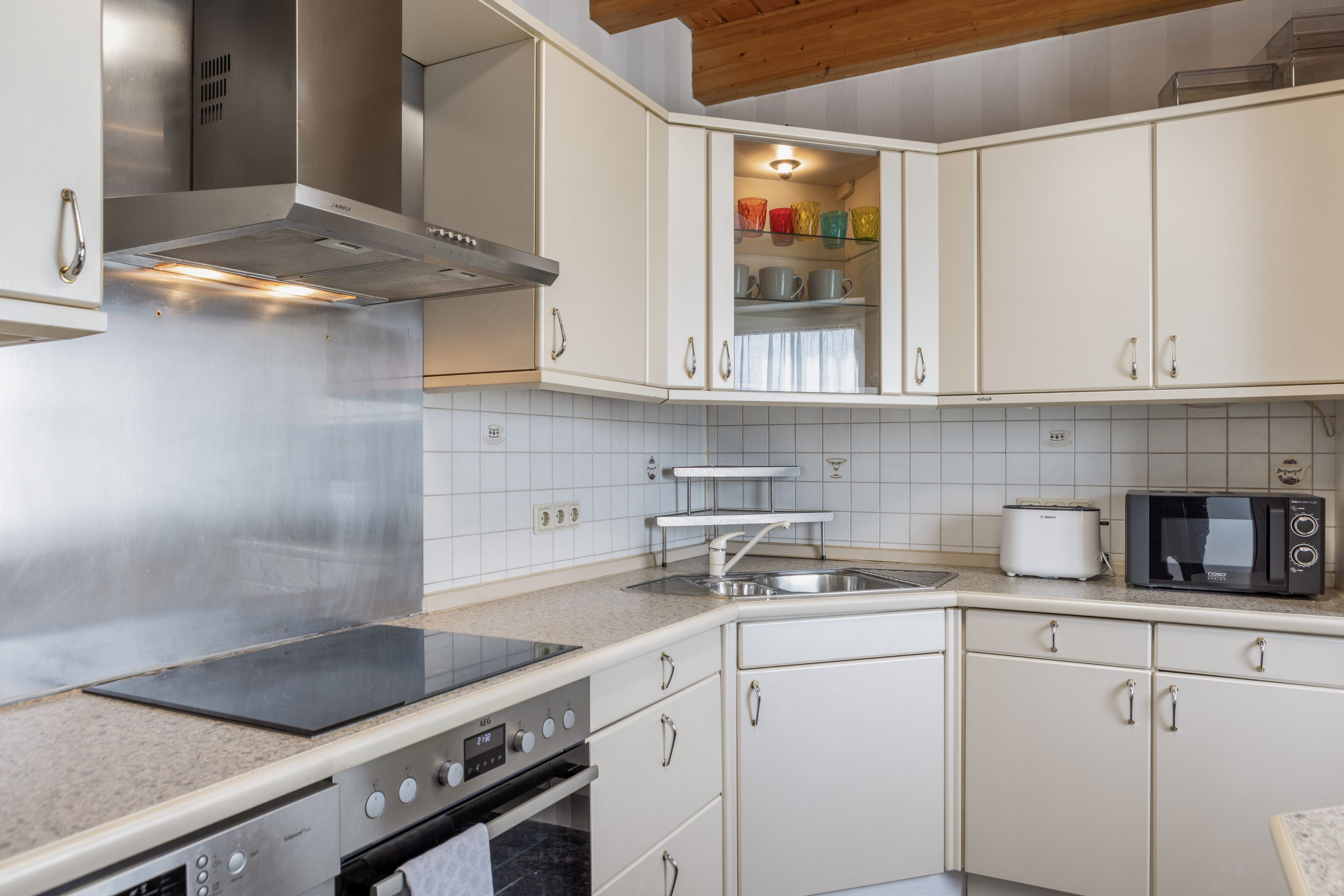 Une cuisine avec des armoires blanches, une hotte de cuisinière en acier inoxydable, un four à micro-ondes Bosch et un grille-pain Bosch.