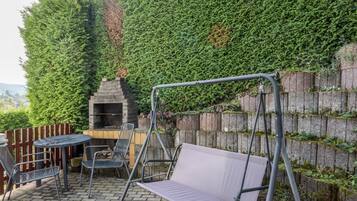 En terrasse med gyngestativ, et rundt bord og grill.
