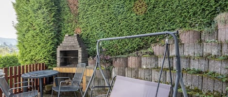 A patio area with a swing set, a round table, and a grill.