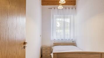 Ein Schlafzimmer mit einem hölzernen Bett, einem Nachttisch, einem Heizkörper und einem Fenster mit durchsichtigen Vorhängen.
