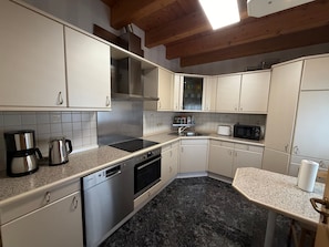 Een keuken met witte kasten, een roestvrijstalen afzuigkap, een vaatwasser, een magnetron en een granieten aanrecht.