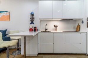 Cozinha moderna com armários brancos, pia de aço inoxidável e chaleira vermelha.