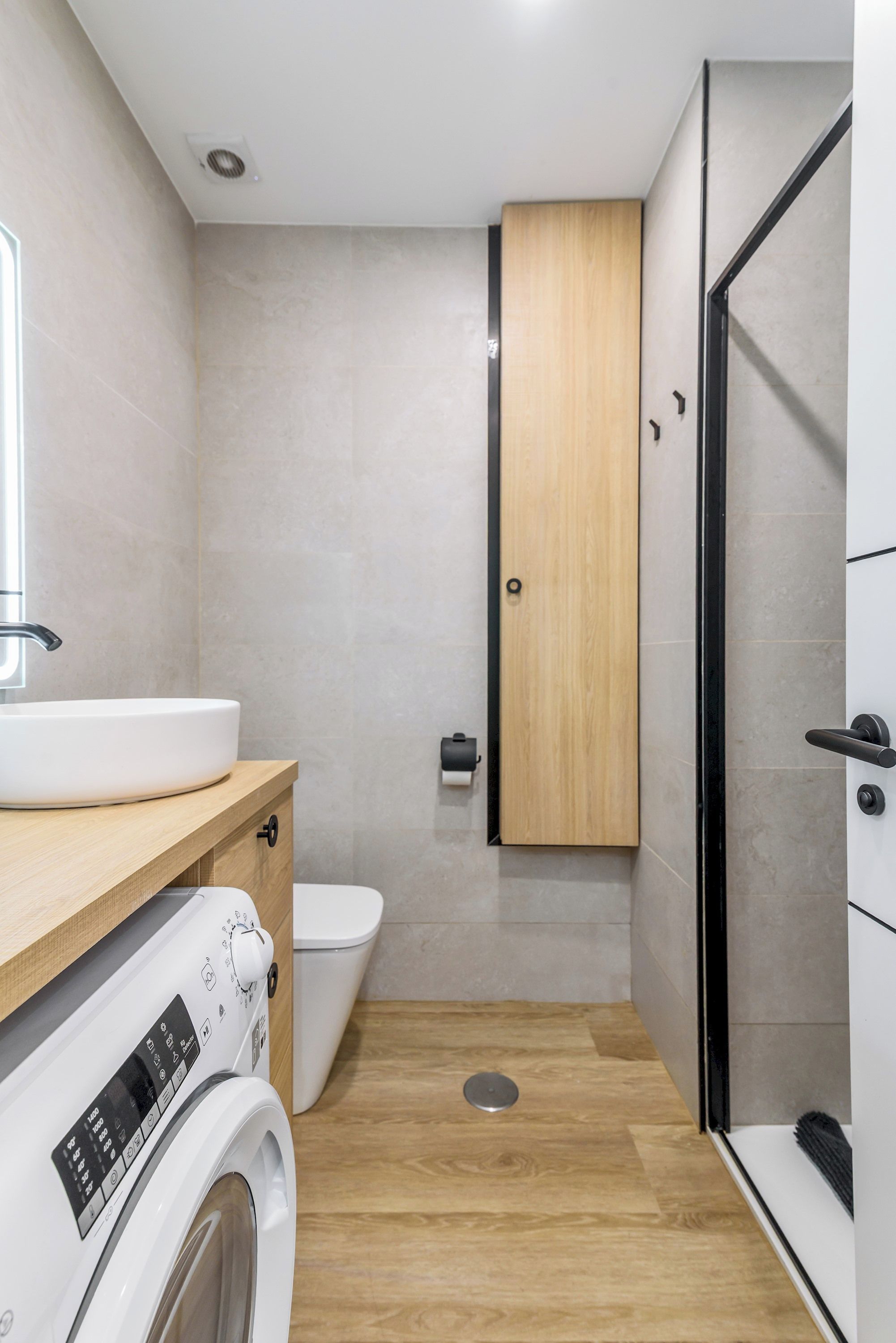 A compact bathroom with a washing machine, toilet, and a shower area.