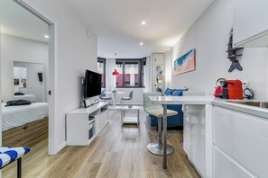 A compact hotel room with a bed, a TV, a dining area with a table and chairs, a kitchenette, and a window with curtains. - Home2Book El Faro by Las Canteras Beach (Las Palmas de Gran Canaria)