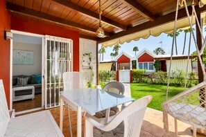 Ein überdachter Patio-Bereich mit Tisch und Stühlen, einer Couch und Blick auf einen Wohnkomplex mit Häusern und Grünflächen.