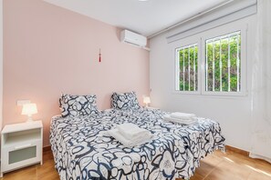Ein Schlafzimmer mit einem Bett, zwei Nachttischen, einem Fenster mit Blick auf Grünflächen und einer Klimaanlage an der Wand.