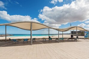 A beachside pavilion with a curved roof, seating, and a view of the ocean. - Home2Book Betty's Chic City Apartment (Puerto del Rosario)