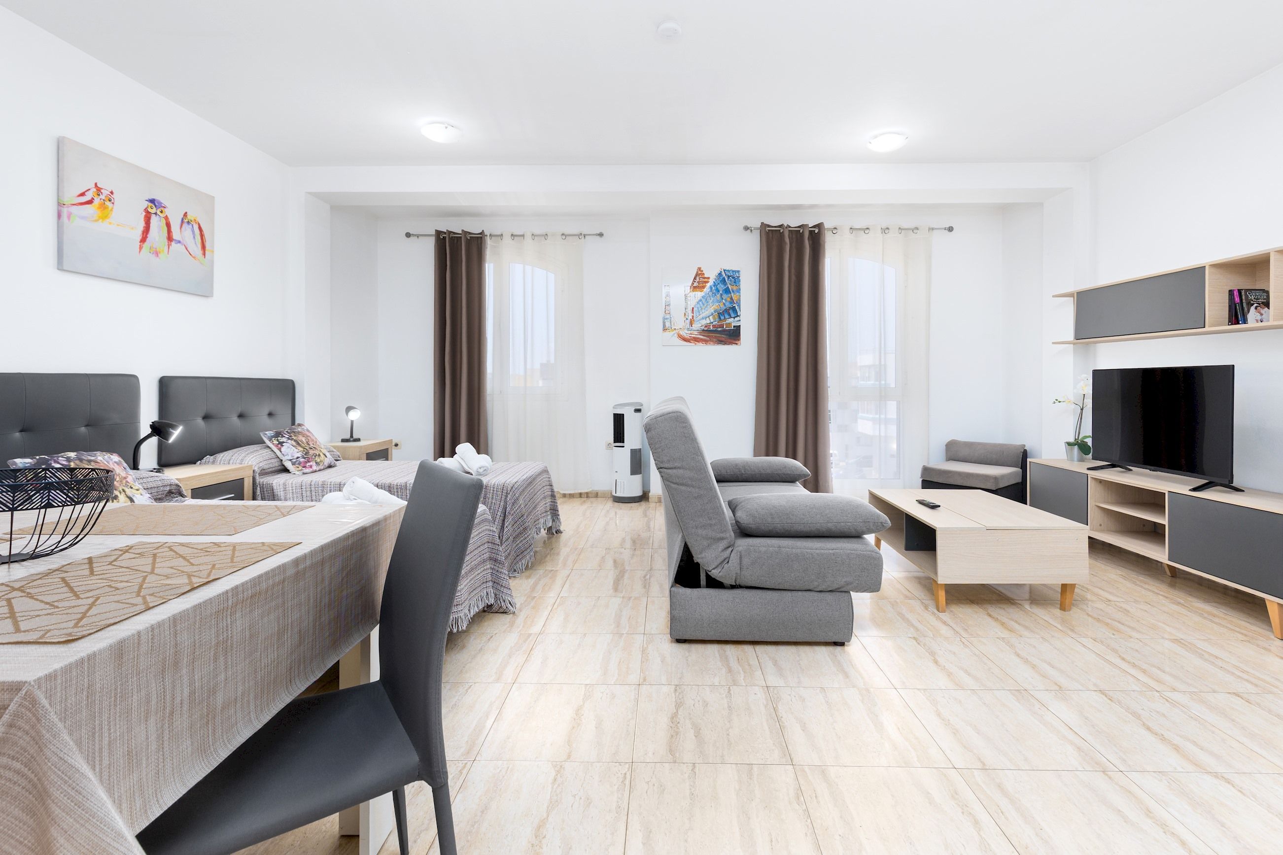 Ett modernt vardagsrum med en soffa, en tv och en matplats med ett bord och stolar.